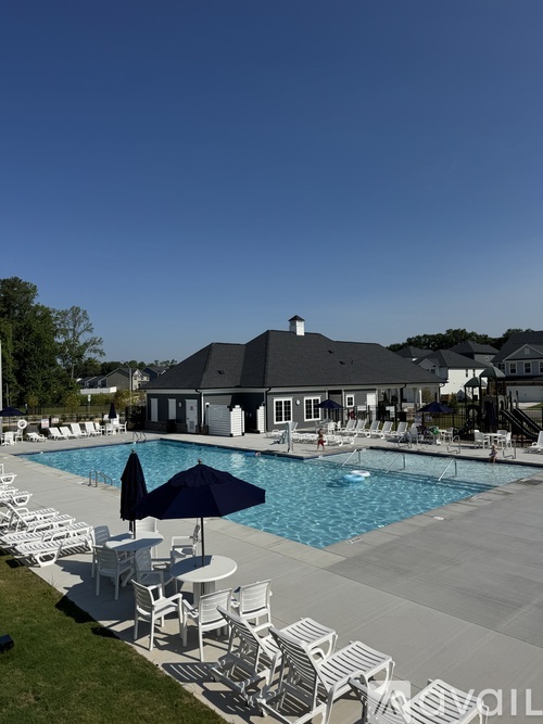 A pool area with chairs and umbrellas in front of a house.