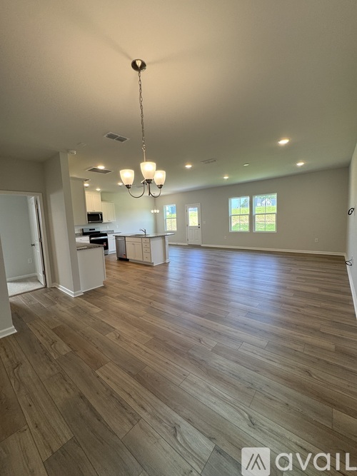A spacious room with wooden flooring and a chandelier hanging from the ceiling.