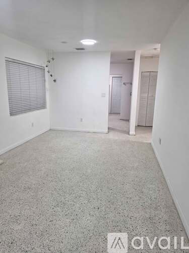 A room with a carpeted floor and a window with blinds.