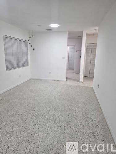 A room with a carpeted floor and a window with blinds.