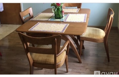 A wooden dining table with four chairs and a vase of flowers on top.