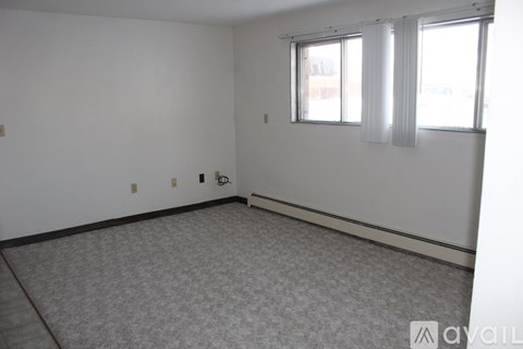A room with a carpeted floor and a window with white curtains.