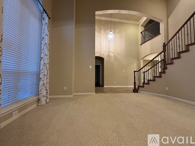 A spacious room with a staircase and a window with blinds.
