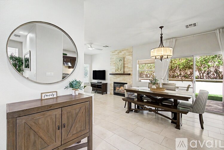 A modern living room with a wooden cabinet, a round mirror, a chandelier, and a dining table with chairs.