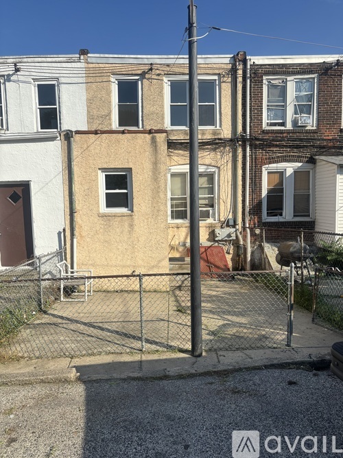 A chain-link fence surrounds a vacant lot with a building in the background.