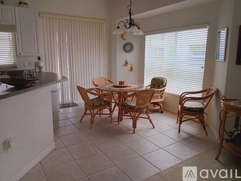 A dining room with a table set for four and a kitchen area with white cabinets.