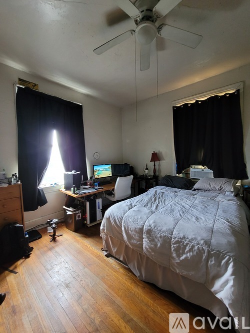A bedroom with a bed, desk, and ceiling fan.