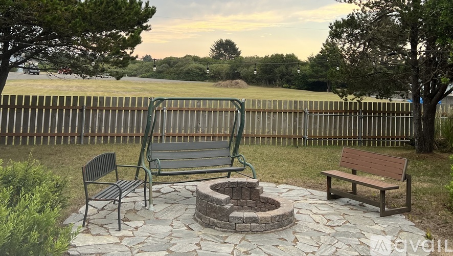 A park bench sits in front of a fence with a fire pit in the middle.