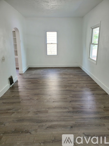 A room with wooden flooring and two windows.