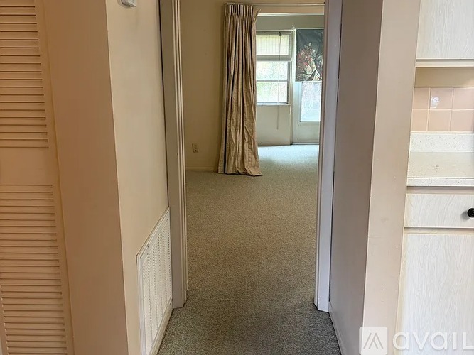 A hallway with a carpeted floor, a doorway, and a window with curtains.