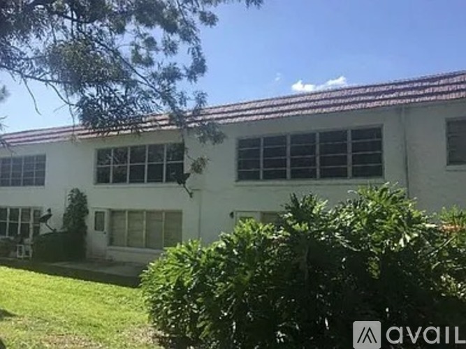 A white building with a red roof and a tree in front.