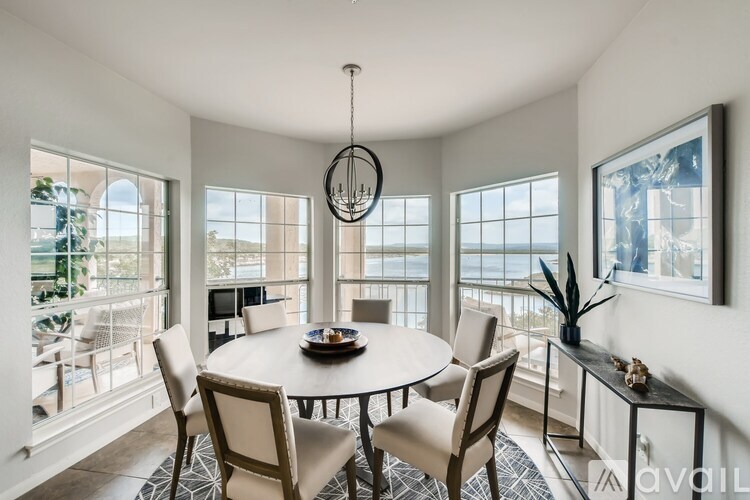 A dining room with a round table and chairs, a chandelier, and a view of the ocean through the windows.