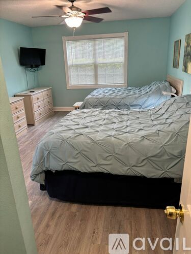 A bedroom with two beds, a ceiling fan, and a television.