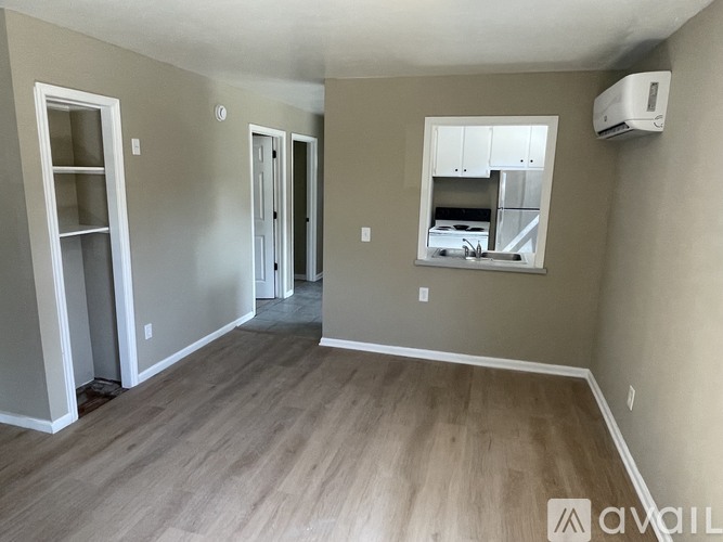 A room with wood flooring and a window overlooking a kitchen.