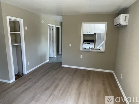 A room with wood flooring and a window overlooking a kitchen.