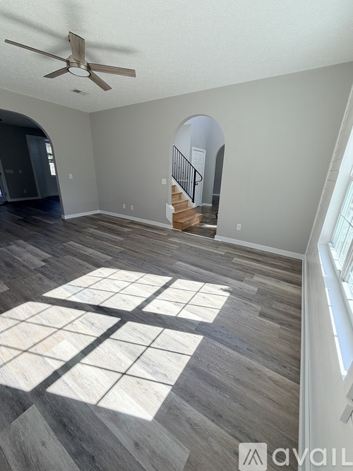 A spacious room with a fan and a staircase in the background.