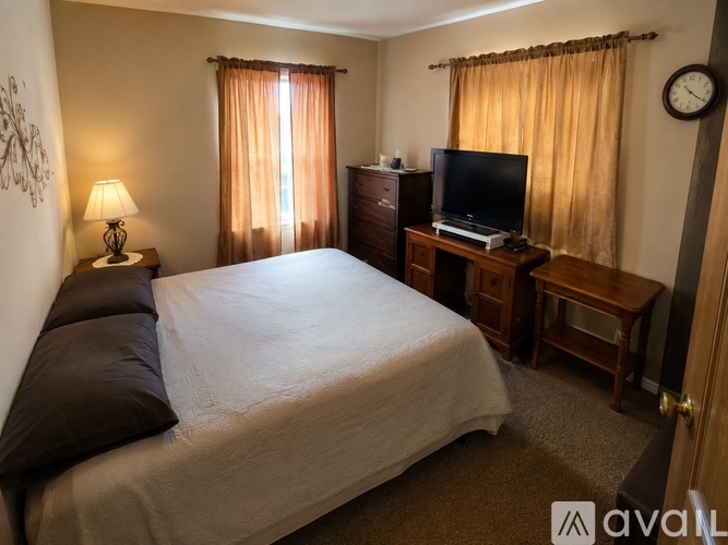 A bedroom with a bed, a desk with a television, and a clock on the wall.