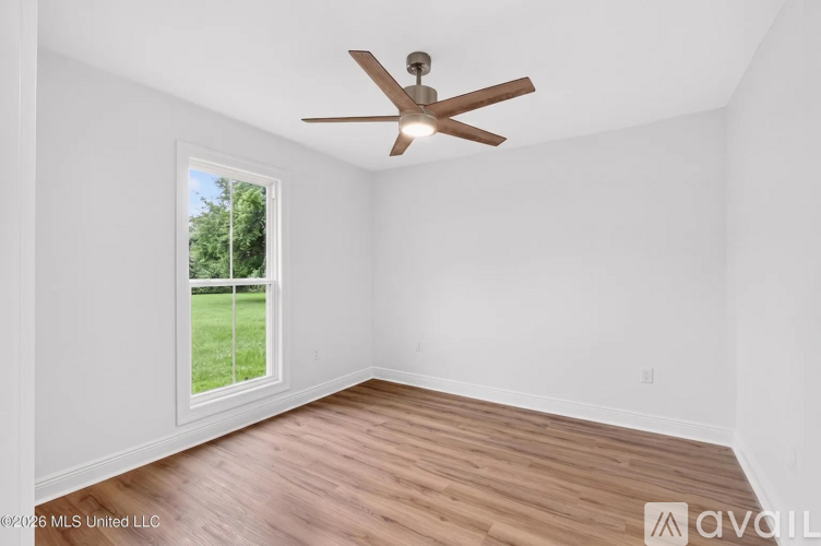 A room with a ceiling fan and a window overlooking a green lawn.