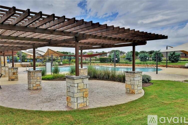 A patio area with a wooden pergola and a pool in the background.