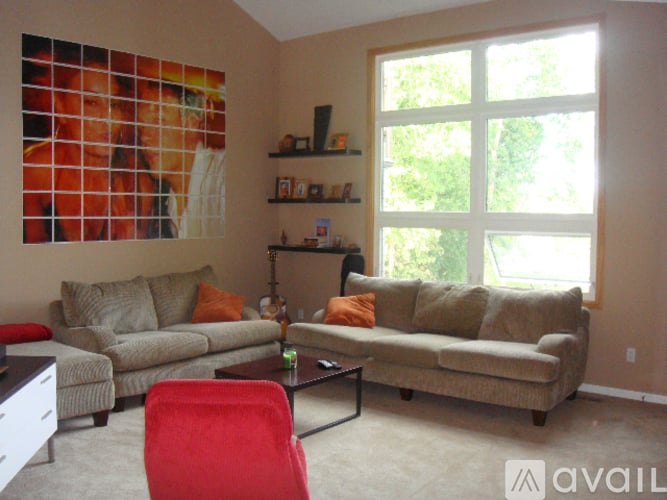 A living room with a red chair and a large picture on the wall.