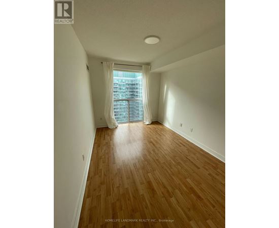 A room with wooden flooring and a window with white curtains.