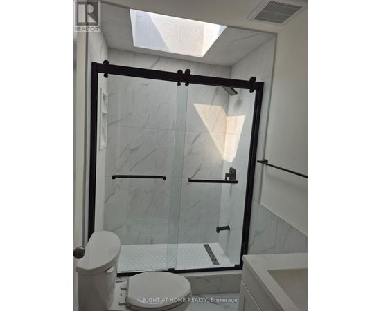 A white toilet sits in a bathroom with a walk-in shower.