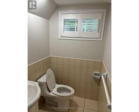 A white toilet in a small bathroom with a window above it.