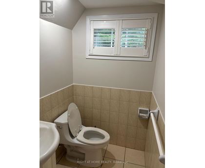 A white toilet in a small bathroom with a window above it.