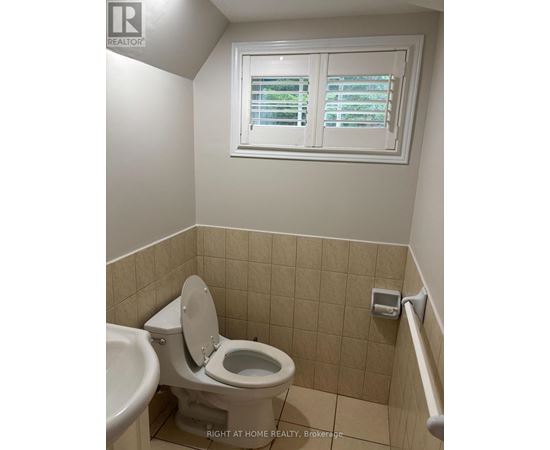 A white toilet in a small bathroom with a window above it.