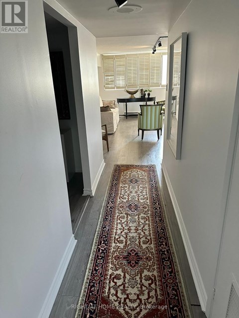 A hallway with a rug on the floor and a living room in the background.