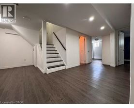 A spacious room with wooden floors and a staircase leading to another level.