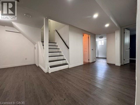 A spacious room with wooden floors and a staircase leading to another level.