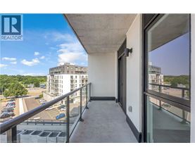 A balcony with a glass door overlooks a parking lot and buildings.