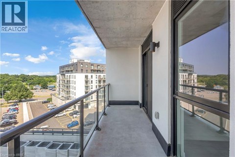 A balcony with a glass door overlooks a parking lot and buildings.