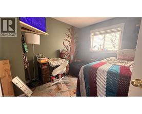 A bedroom with a bed covered in a multicolored blanket, a desk with a lamp, and a window with blinds.