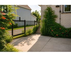 A black metal fence separates a sidewalk from a green bush.
