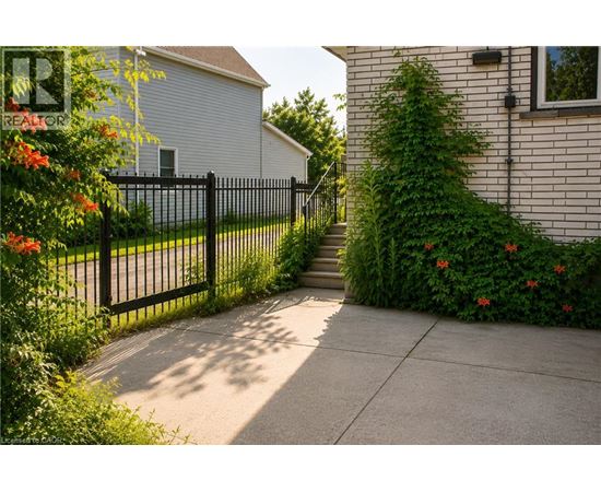 A black metal fence separates a sidewalk from a green bush.