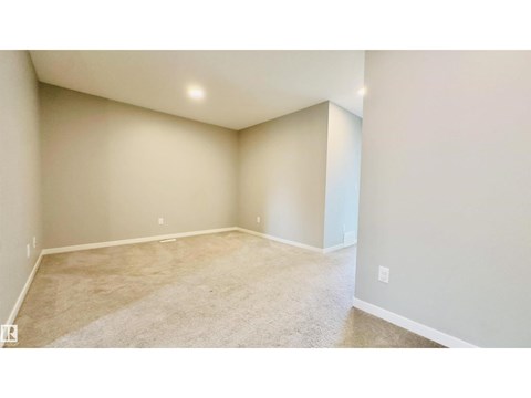A spacious room with beige carpeting and white walls.
