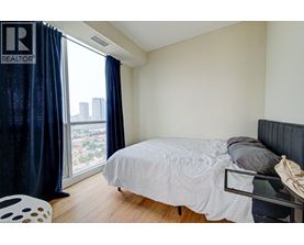A bedroom with a bed, chair, and window with a view of the city.