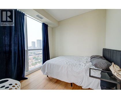 A bedroom with a bed, chair, and window with a view of the city.
