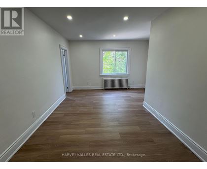 A room with wooden flooring and a window with a view of trees outside.