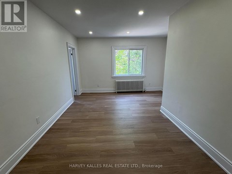 A room with wooden flooring and a window with a view of trees outside.