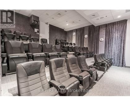 A row of black cinema seats are empty and facing a screen.