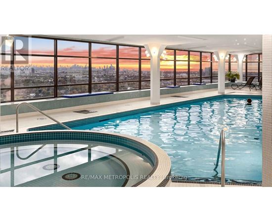 A swimming pool in a room with a view of the city at sunset.