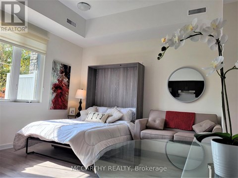 A bedroom with a bed, a couch, and a round mirror on the wall.
