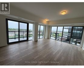 A spacious room with wooden flooring and large windows overlooking a cityscape.