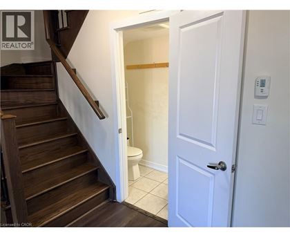 A white door is open to a bathroom with a toilet and a wooden staircase.