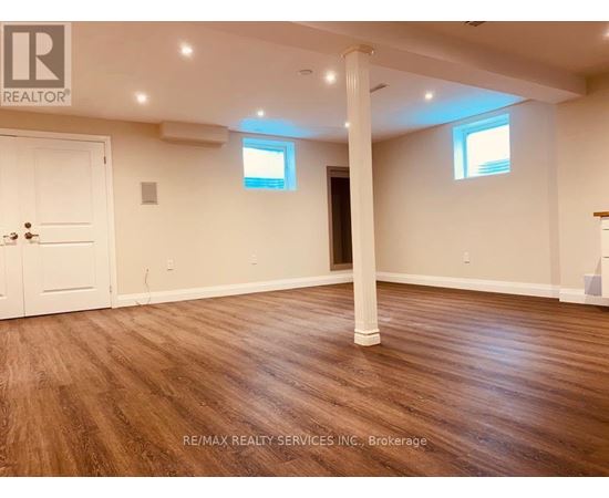 A room with wooden flooring and white walls, with a door on the left and a window on the right.