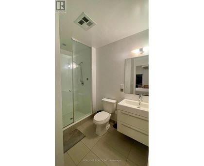 A white toilet sits in a bathroom next to a sink and a glass shower stall.