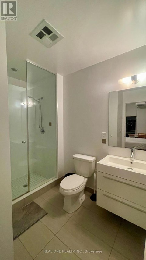 A white toilet sits in a bathroom next to a sink and a glass shower stall.